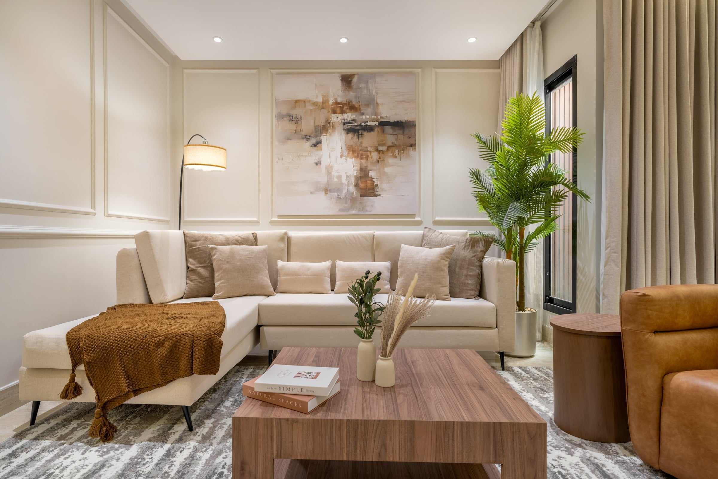 Living room with a cream corner sofa, a walnut coffee table and an abstract painting on panelled walls, Riyadh apartment