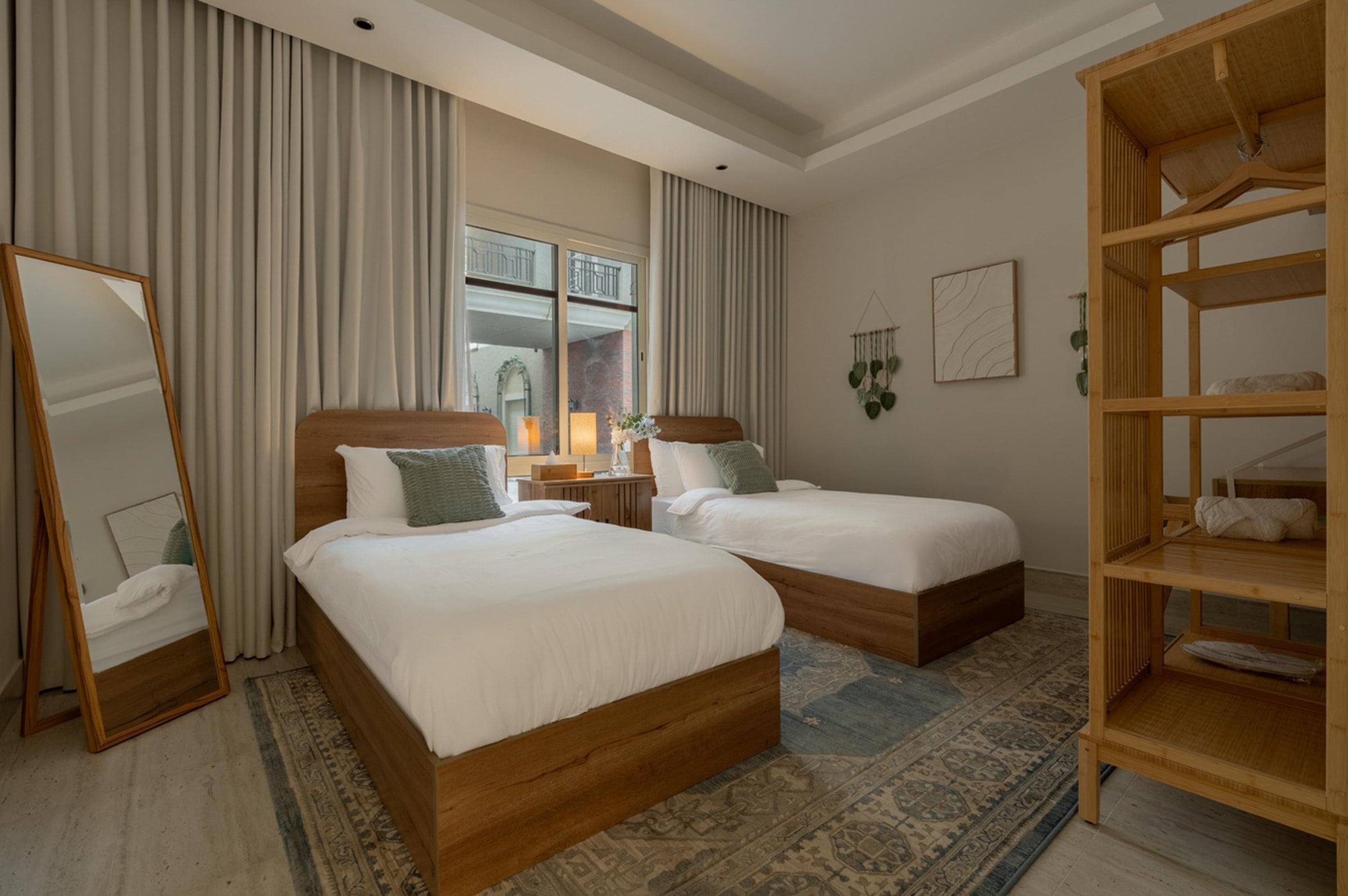 Bedroom with two single wood beds, sage cushions, a floor mirror and an open bamboo wardrobe, Riyadh apartment